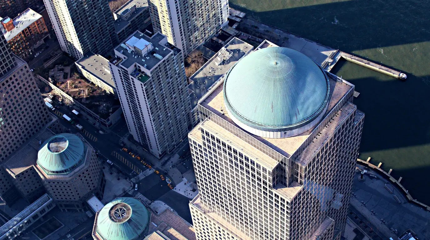 Aerial view of financial-district towers with green copper domes beside the river.