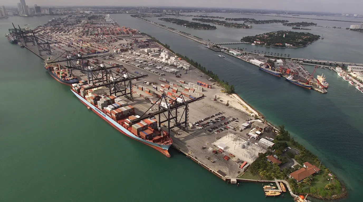 Aerial view of a container port on an island, cranes loading a container ship beside the stacked terminal yard.