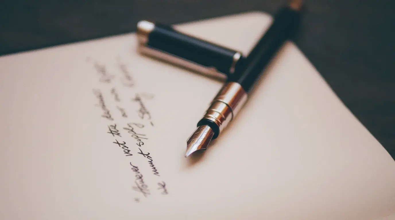 A fountain pen and its cap lying on a handwritten letter on cream paper.