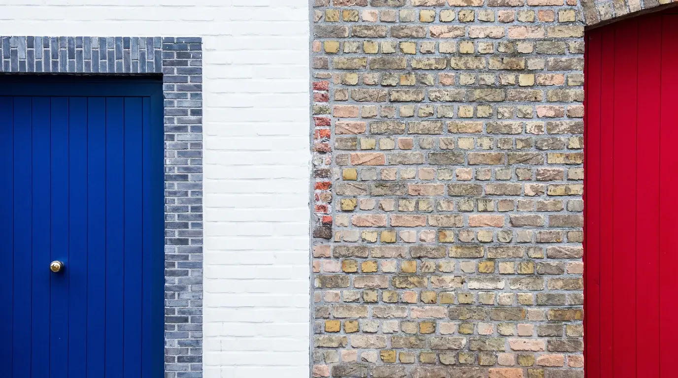 A bright blue front door and a red door set in a brick and painted-brick wall.