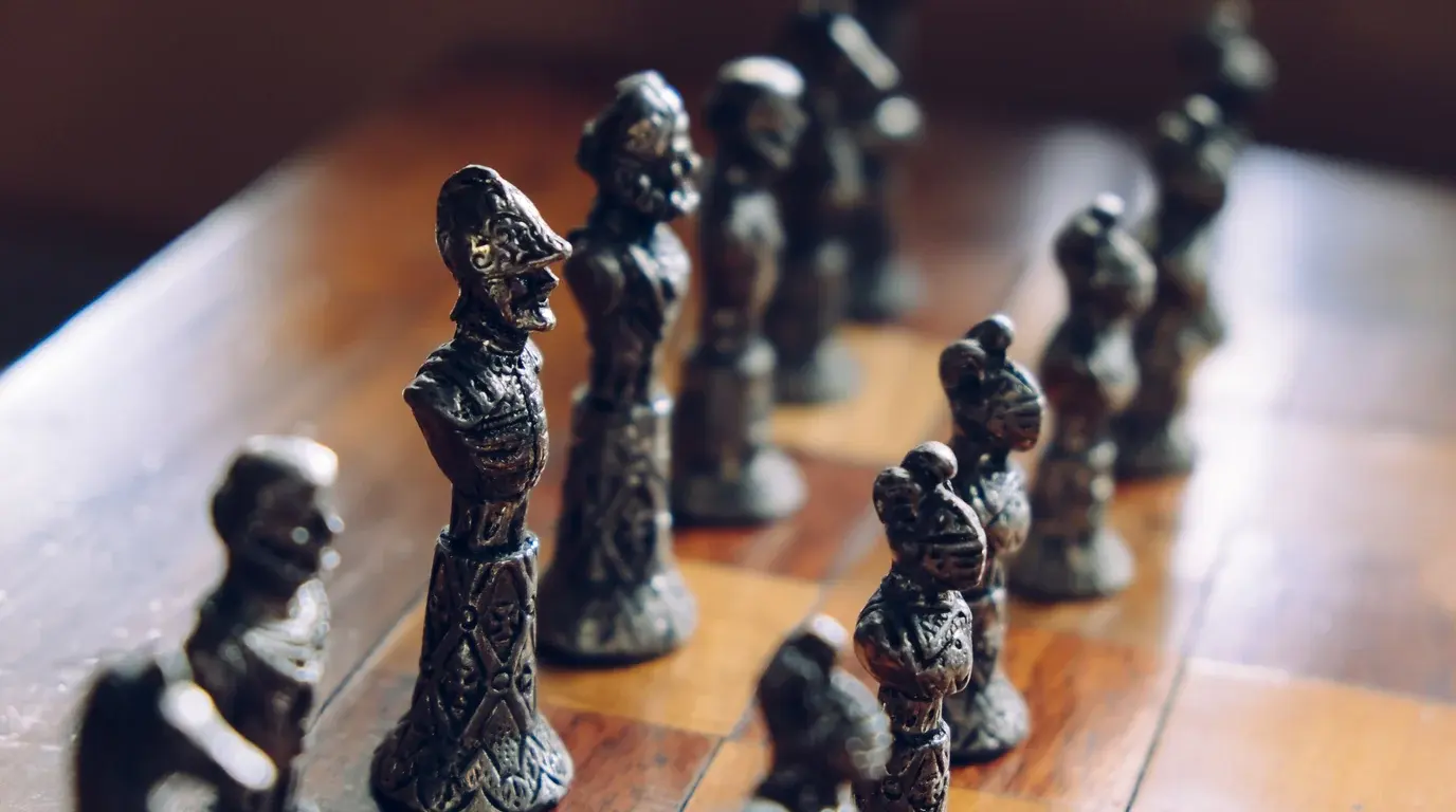 Ornate vintage metal chess pieces lined up on a polished wooden chessboard.