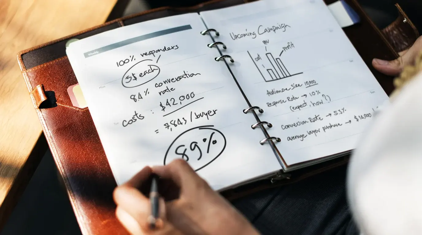 A hand writing campaign figures and a 89% conversion note in a leather-bound planner.