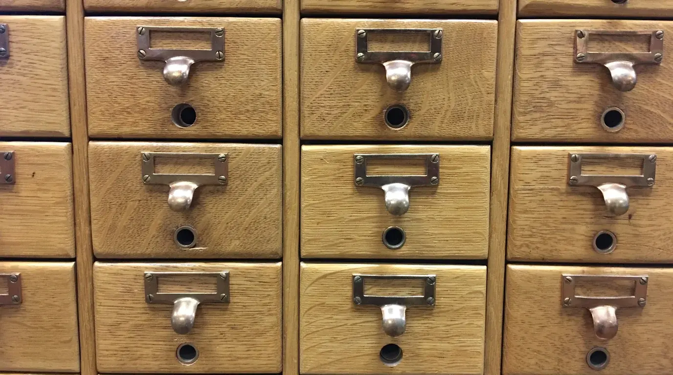 Rows of oak card-catalogue drawers with brass label holders and pull handles.