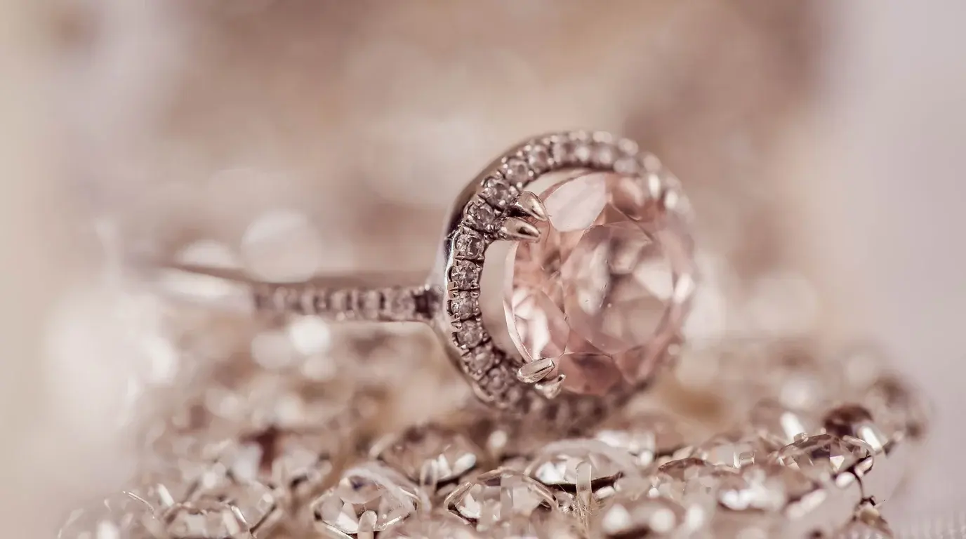 A pink gemstone ring with a halo of small diamonds resting on a pile of sparkling jewellery.