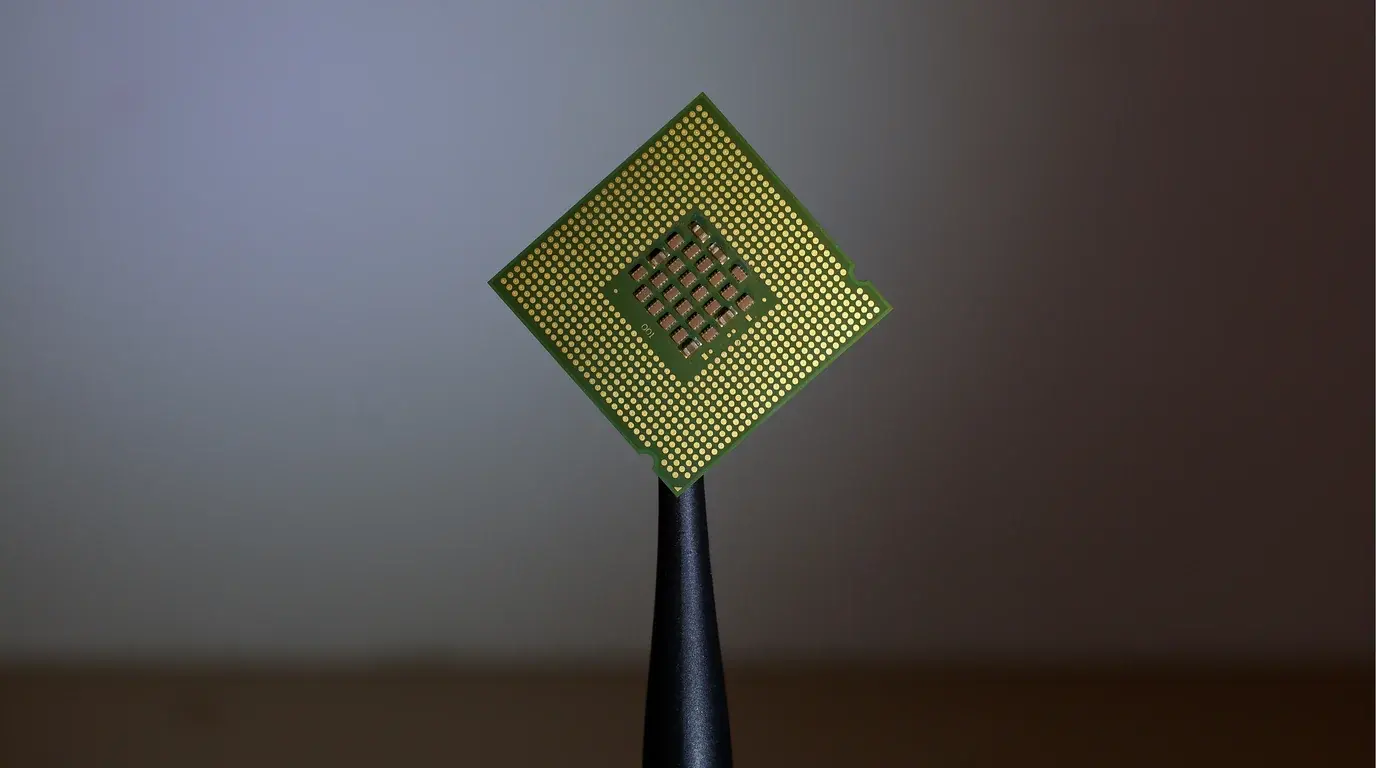 A single processor chip held up on a dark stand, its gold contact grid catching the light.