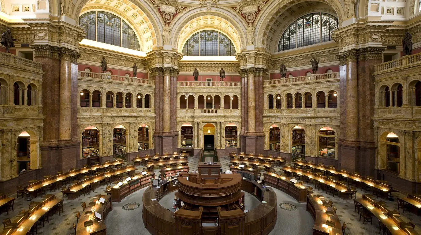 The Main Reading Room of the Library of Congress, circular rows of wooden reading desks beneath arched windows.