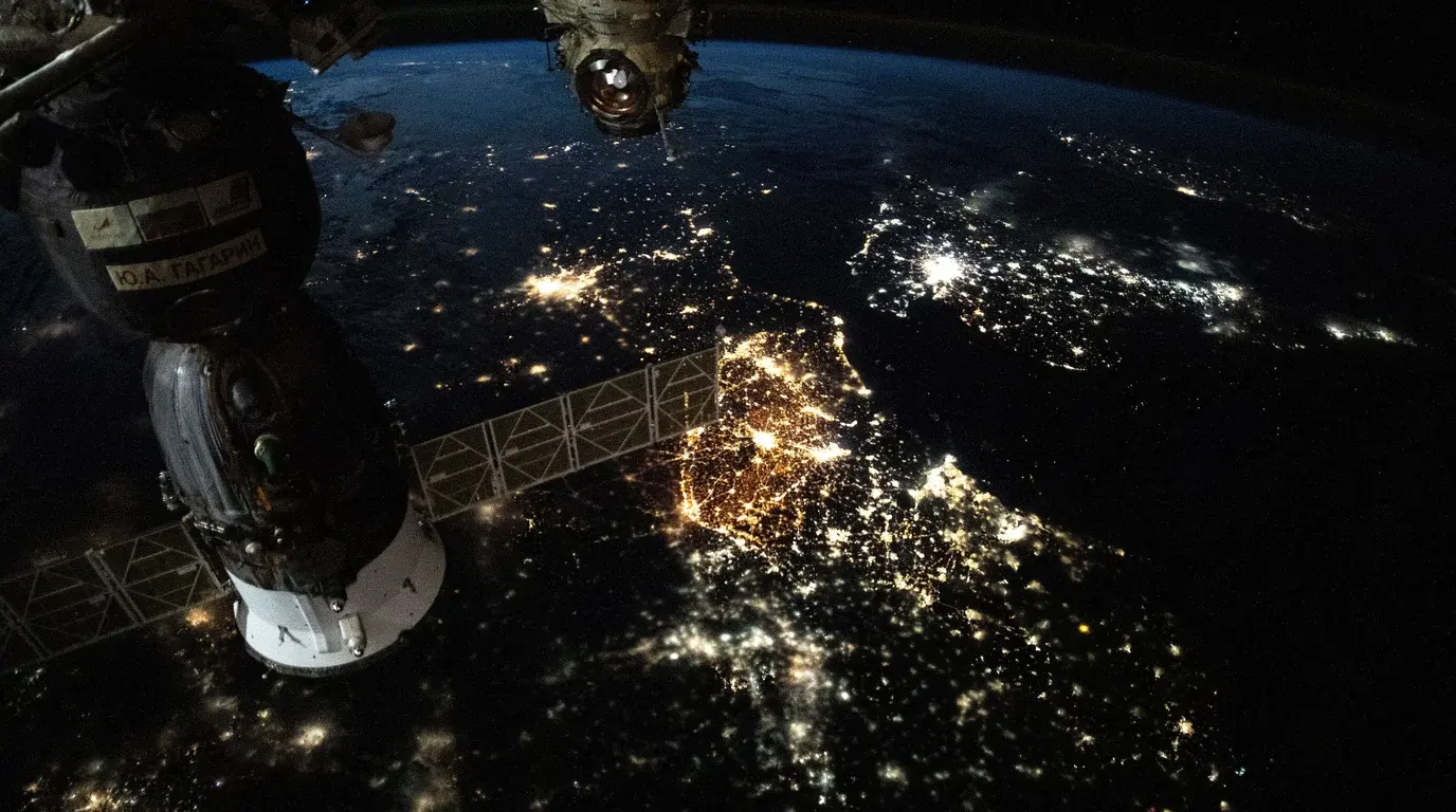 Europe at night seen from the International Space Station, city lights spread below a docked Soyuz spacecraft and its solar array.