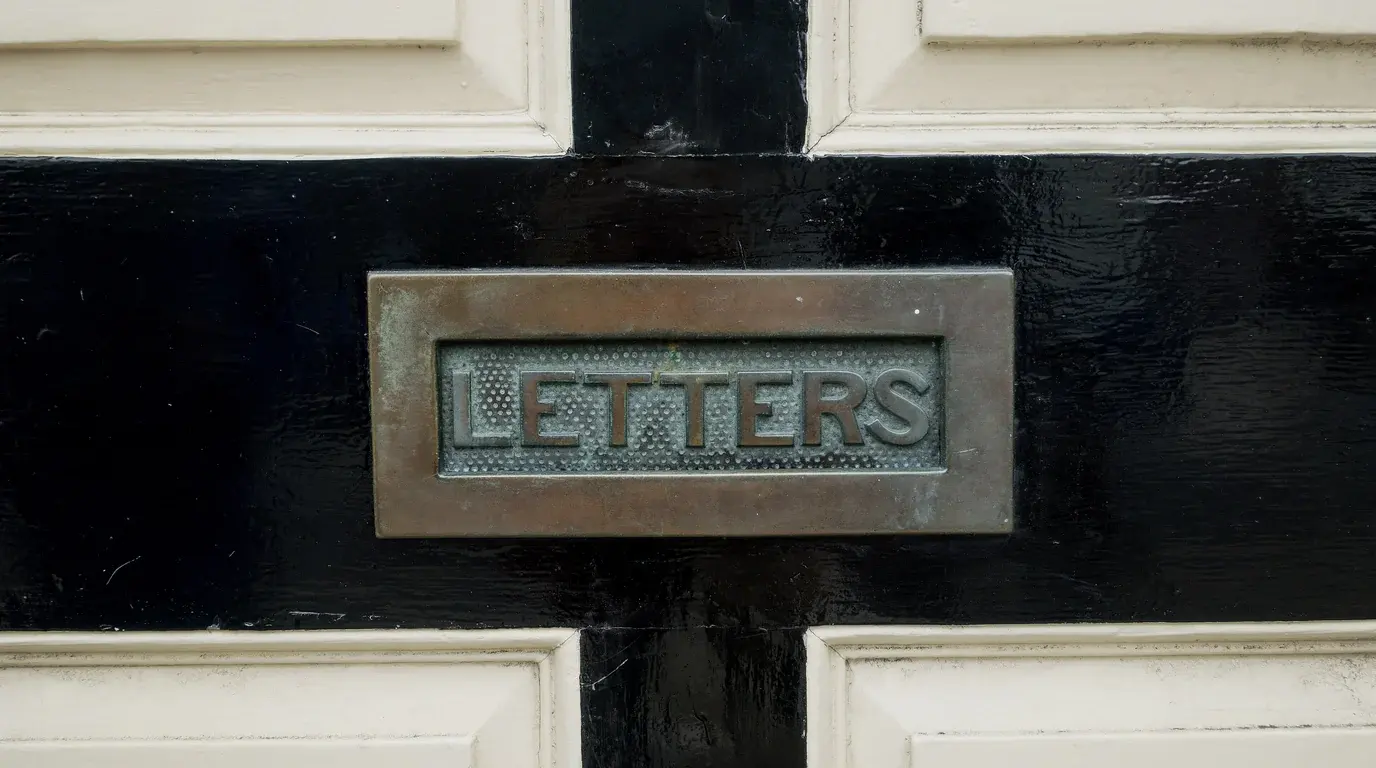 A brass letterbox plate engraved LETTERS set in a glossy black door between cream panels.