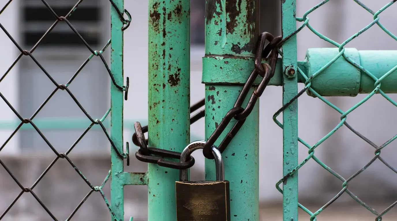 A padlock and chain securing a weathered turquoise gate in a chain-link fence.