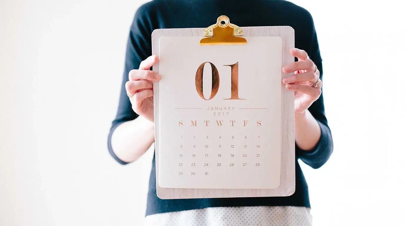 A person in a dark sweater holding a clipboard calendar page showing a large gold 01.