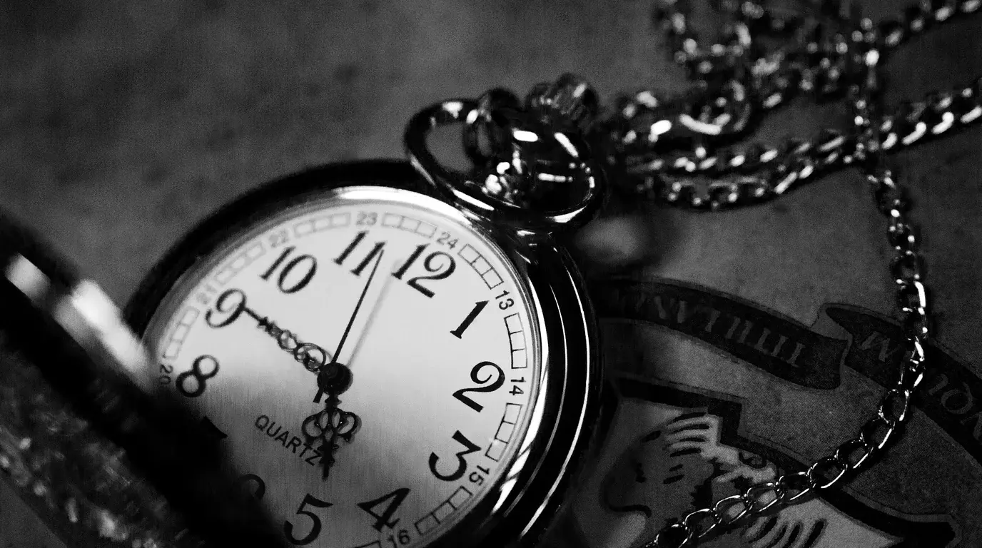 Black-and-white close-up of an open pocket watch, its hands just short of noon, the chain coiled around it.
