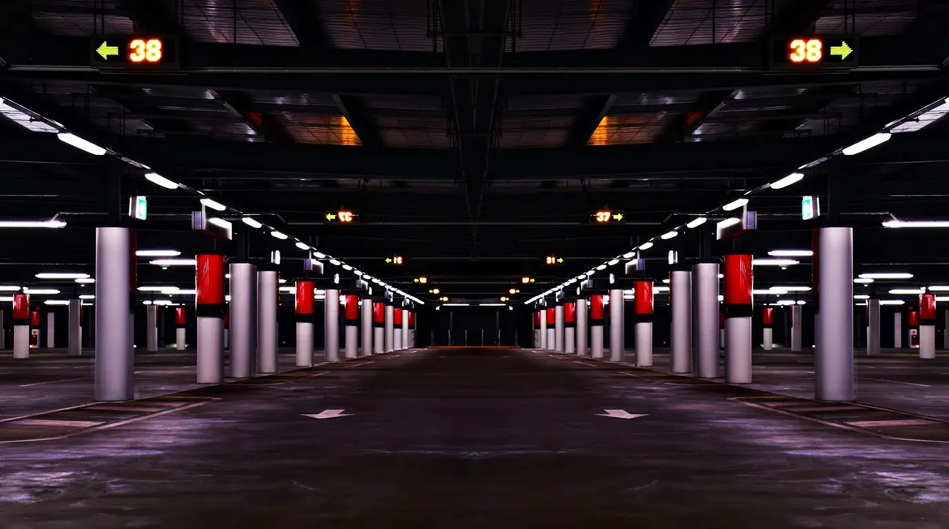 An empty underground car park lit by strip lights, red-banded pillars and illuminated space counters.