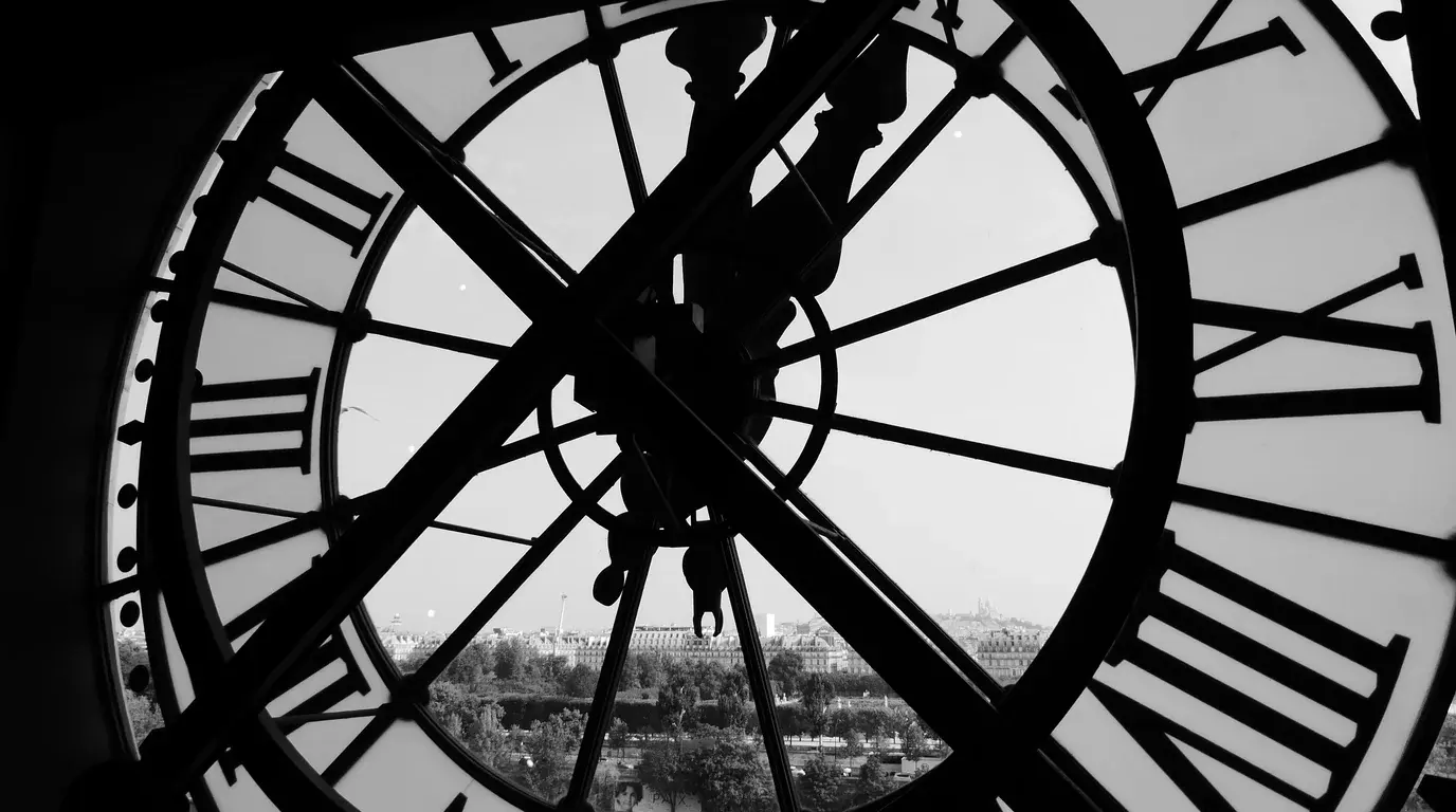 Silhouette of a giant clock face with Roman numerals, a city skyline visible through the glass.