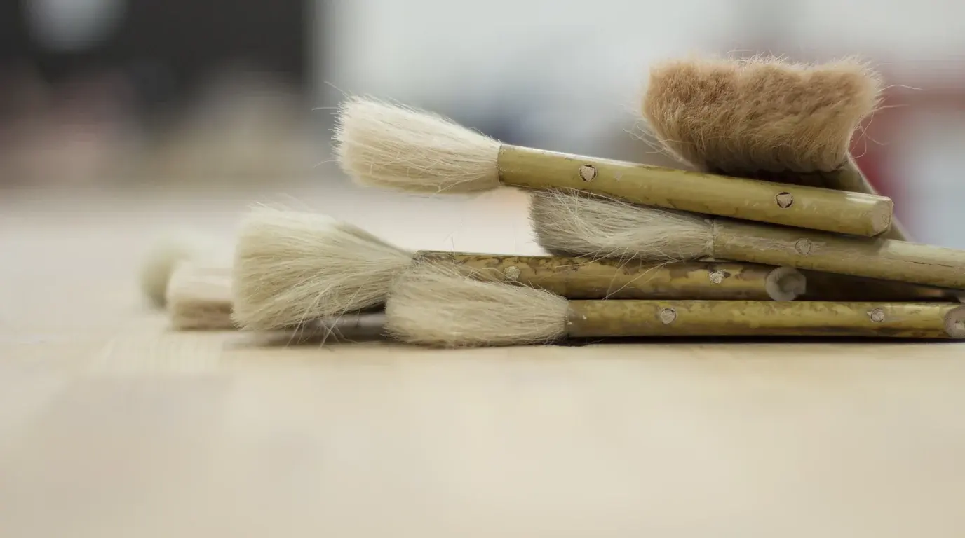 A small pile of natural-bristle paintbrushes with bamboo handles on a pale table.