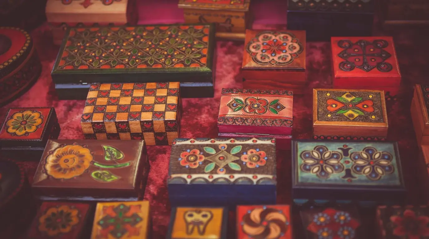 Rows of hand-painted wooden boxes with folk-art patterns laid out on a market table.