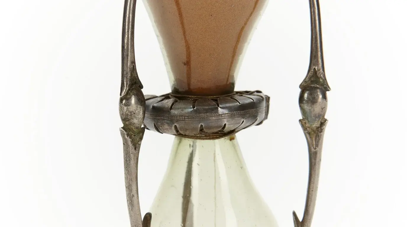 Close-up of an antique silver-framed hourglass, sand running through its narrow glass waist.