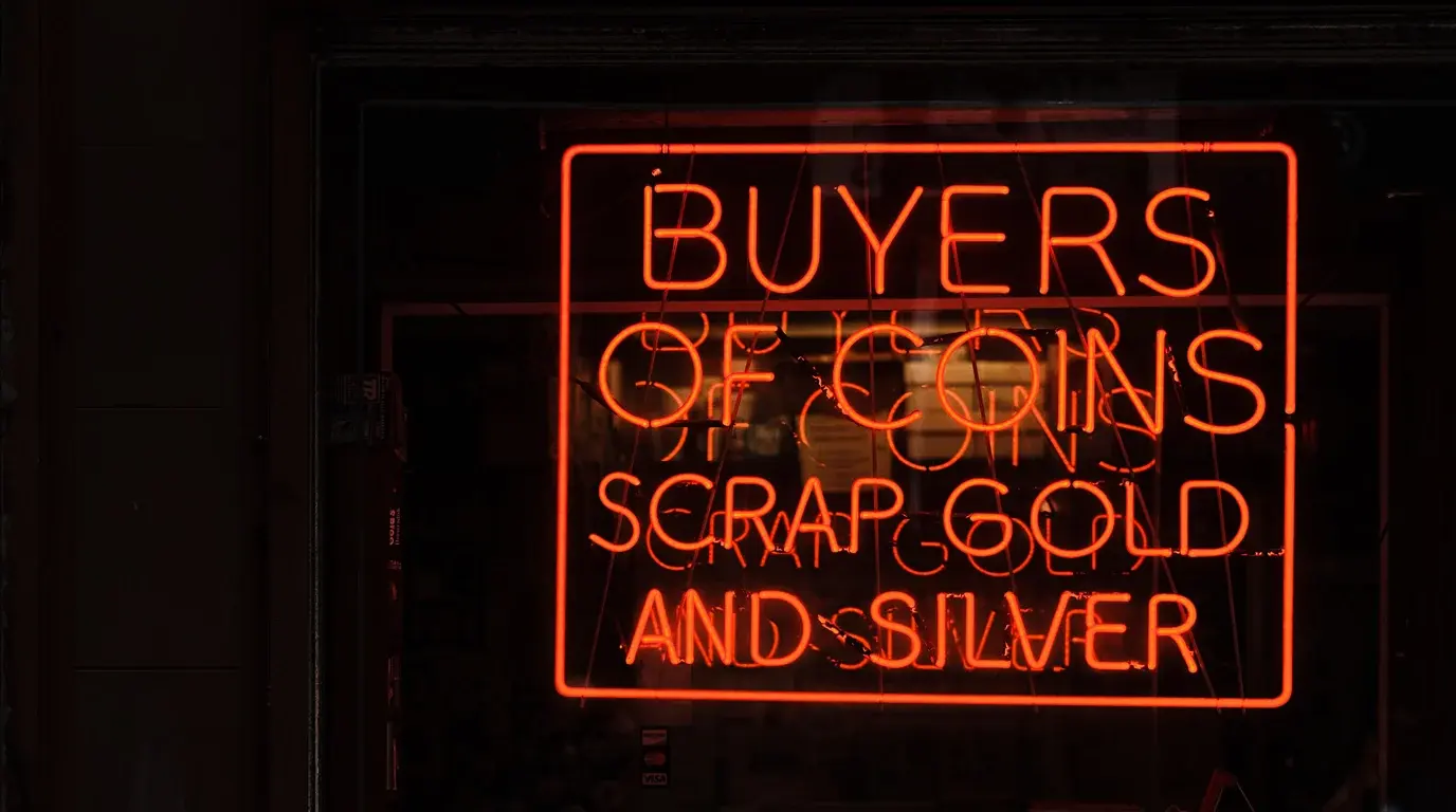 A red neon shop sign reading Buyers of Coins, Scrap Gold and Silver glowing in a dark window.