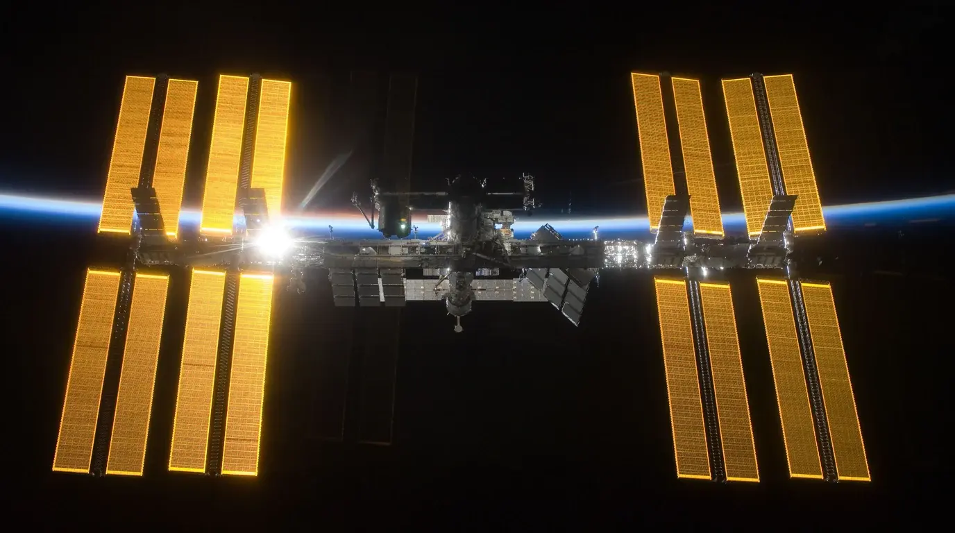 The International Space Station with its golden solar arrays fully extended above Earth's blue horizon.