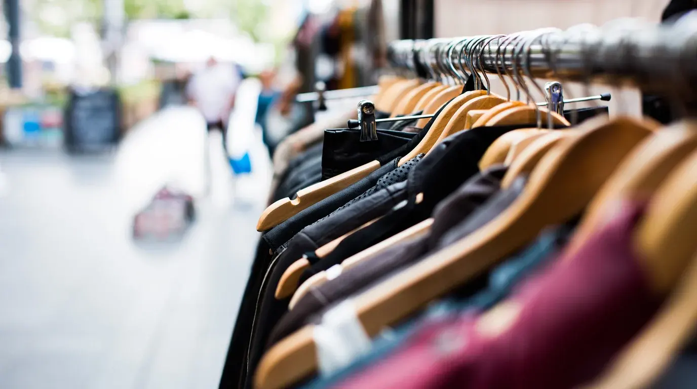 A rail of jackets on wooden hangers at an outdoor clothing stall, the street blurred behind.