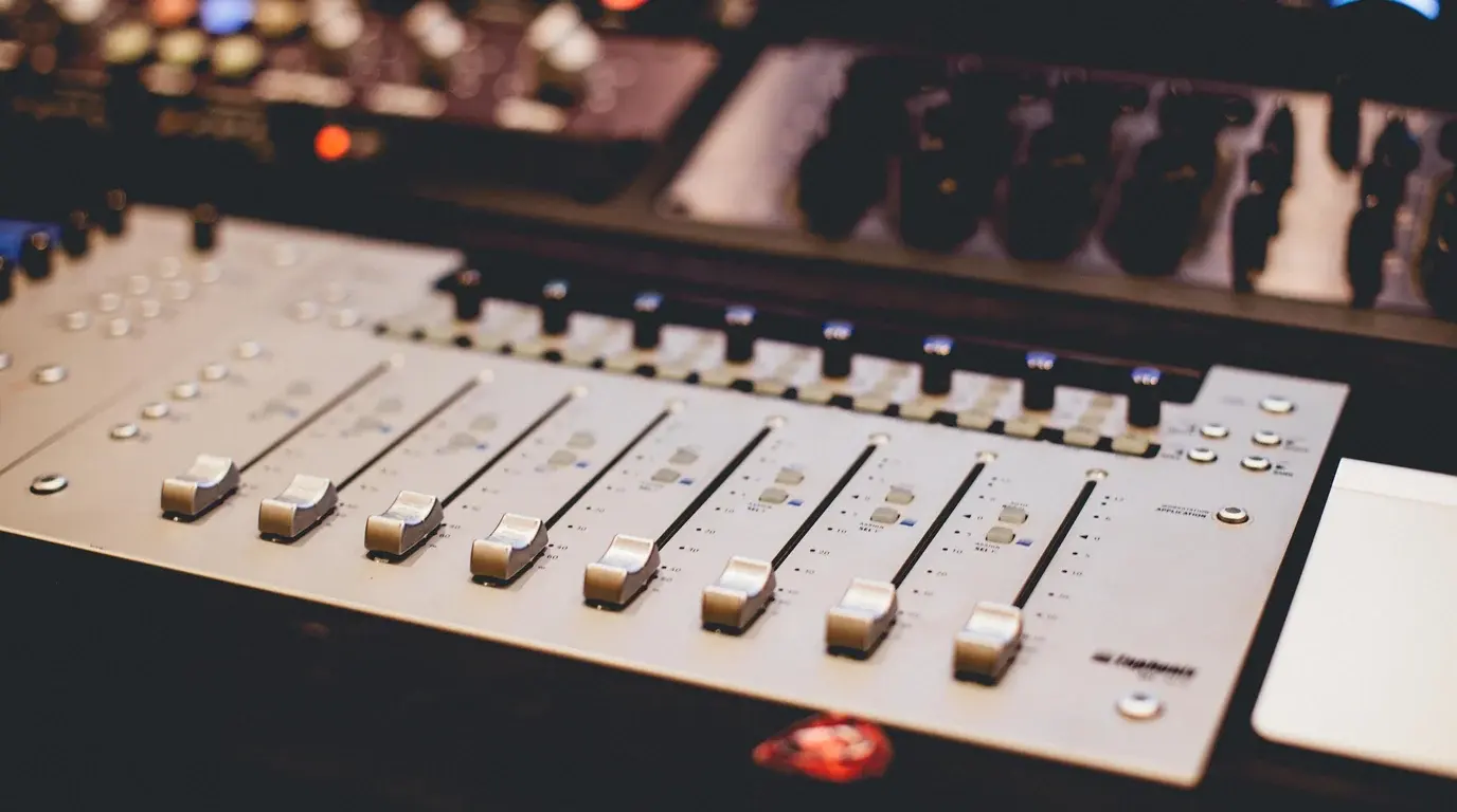 The faders and illuminated buttons of an audio mixing console, close up.