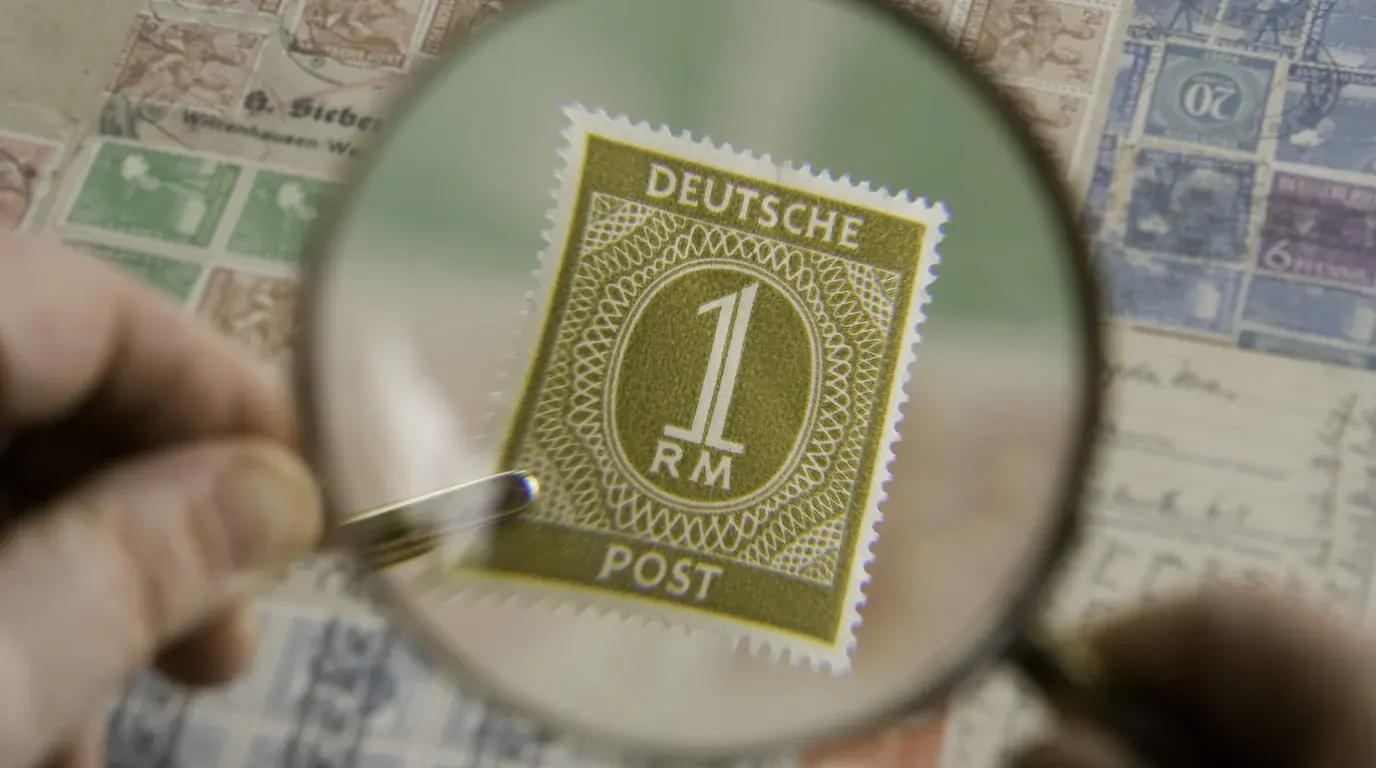 A magnifying glass held over a postage stamp on a page of stamps, checking its details.